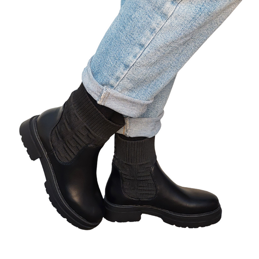 Woman's foot wearing comfortable black chunky pull-on Chelsea ankle boots in faux leather, a versatile choice for London life.
