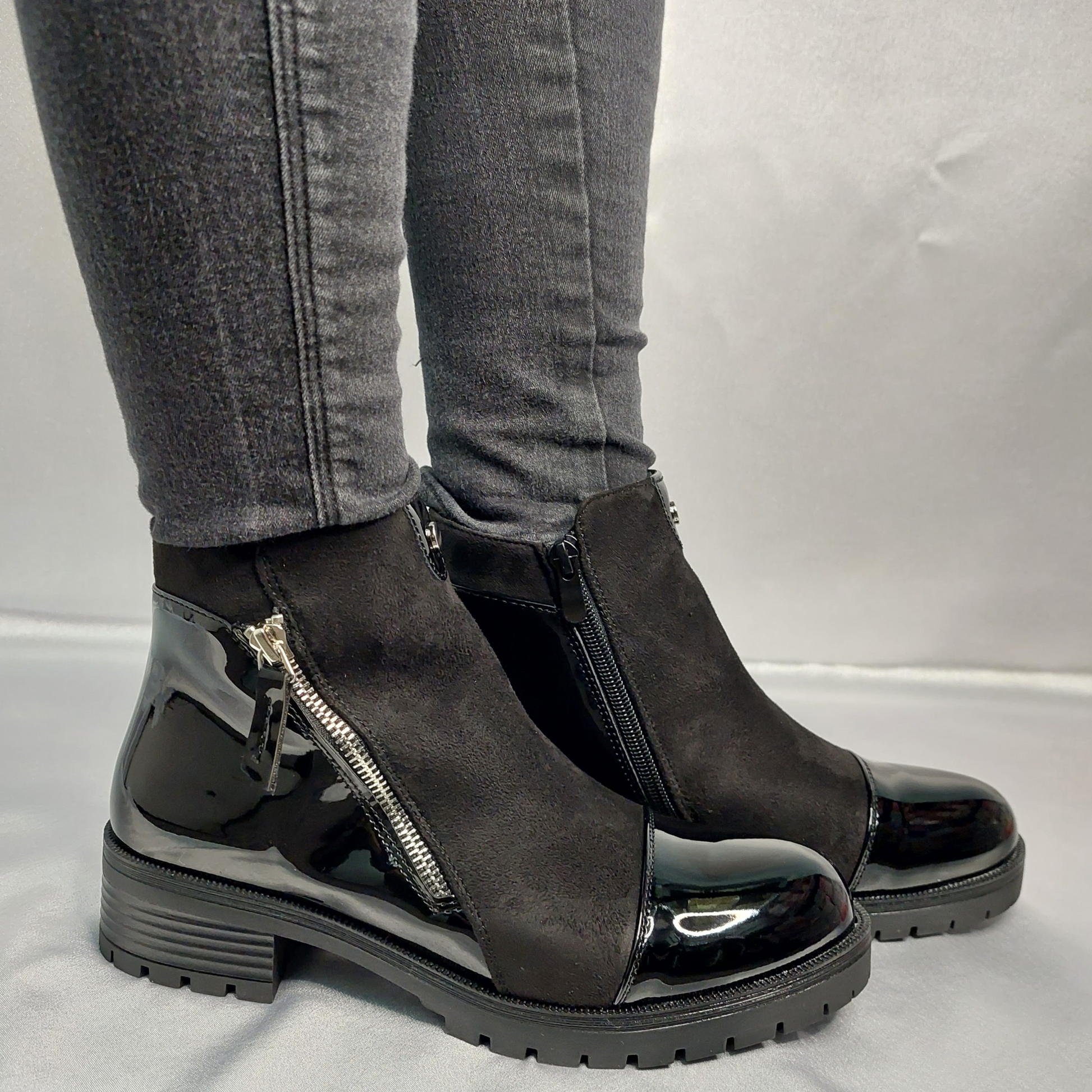 Woman's foot wearing stylish black suede and patent chunky Chelsea ankle boots with a zip pattern, a confident and fashionable choice for London life.