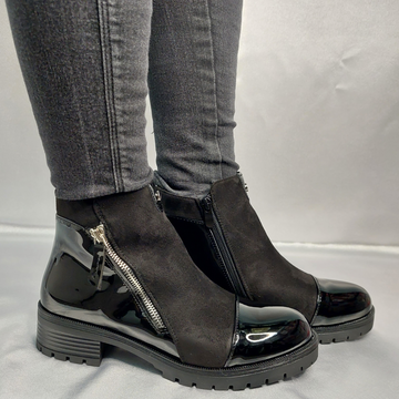 Woman's foot wearing stylish black suede and patent chunky Chelsea ankle boots with a zip pattern, a confident and fashionable choice for London life.