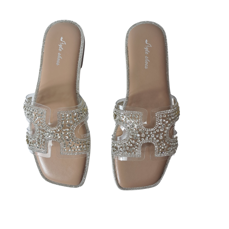 Woman's foot wearing stylish diamante cut-out strap flat summer sandals in silver, a fashionable and comfortable choice for a sunny day in London.