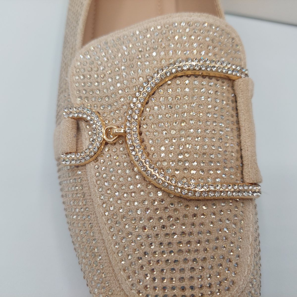 Close-up of the diamante glitter and gold metal decor on women's beige loafers, emphasizing their refined style in London.