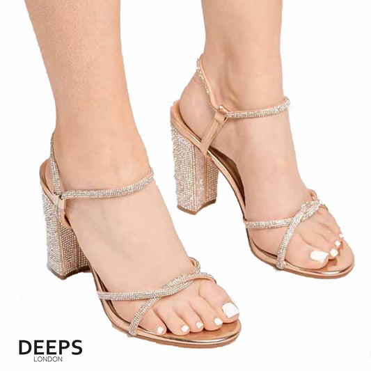 Woman's foot wearing stylish block heel sandals with diamante detail on the heel and strap, featuring a buckle, in rose gold, a fashionable choice for London events from DeepsLondon.