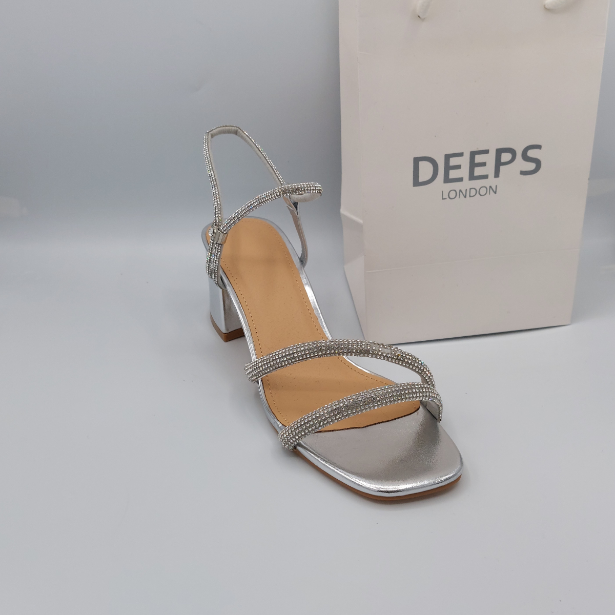 Woman's foot wearing stylish glitter block heel sandal in silver with diamante front straps and buckle ankle strap, a comfortable and fashionable choice from DeepsLondon.