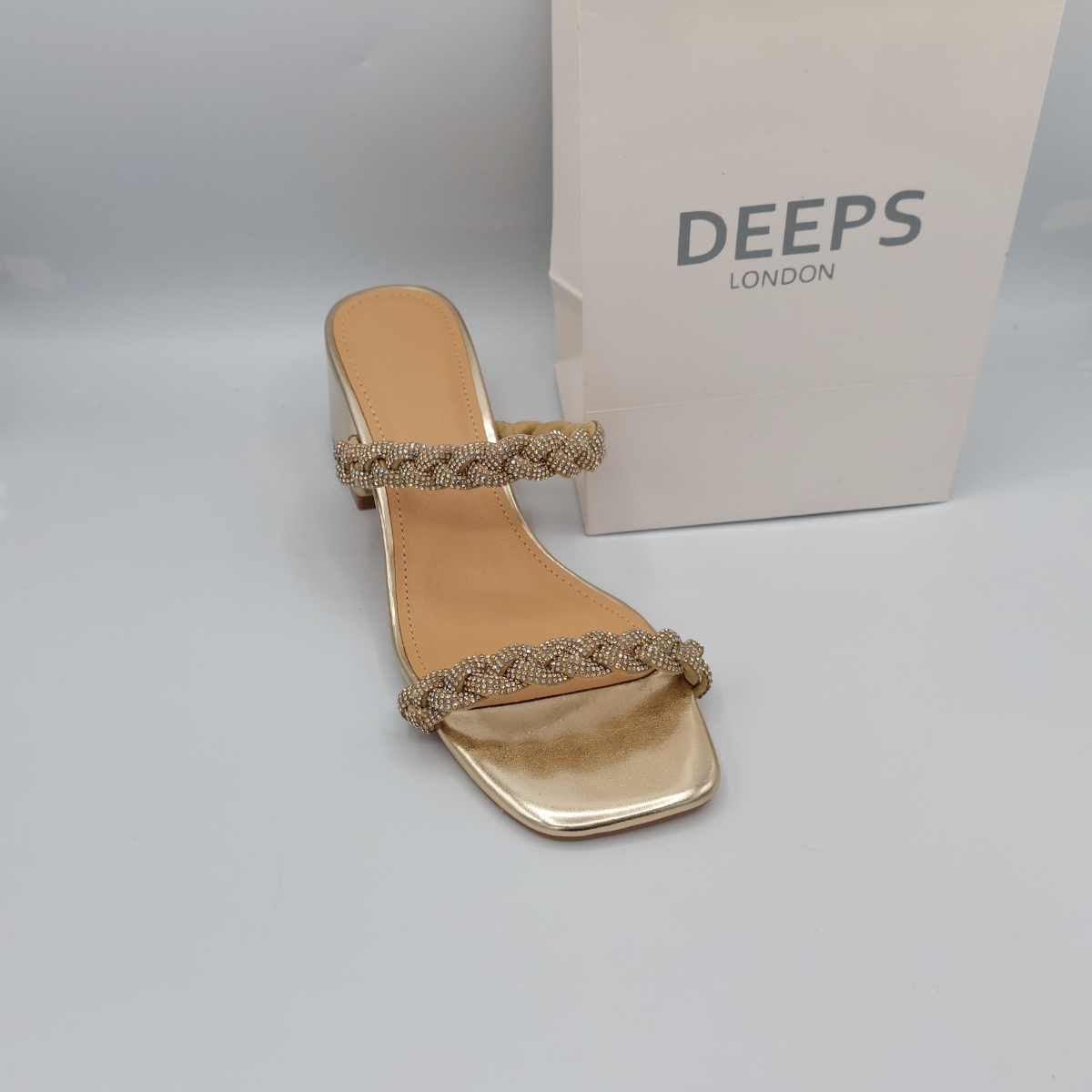 Woman's foot wearing stylish Deeps London gold plaited gemstone band block heel mule, a comfortable and fashionable choice for London events.