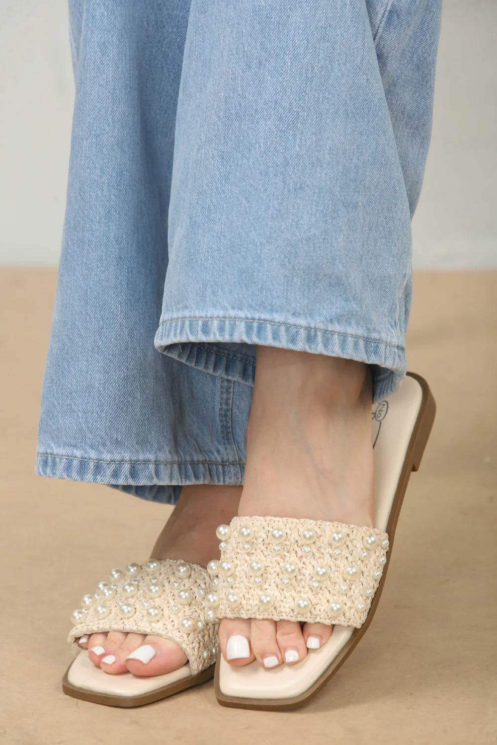 Close-up of the pearl embellishments on flat sandals in cream, emphasizing the delicate sparkle and intricate design, London footwear from DeepsLondon.