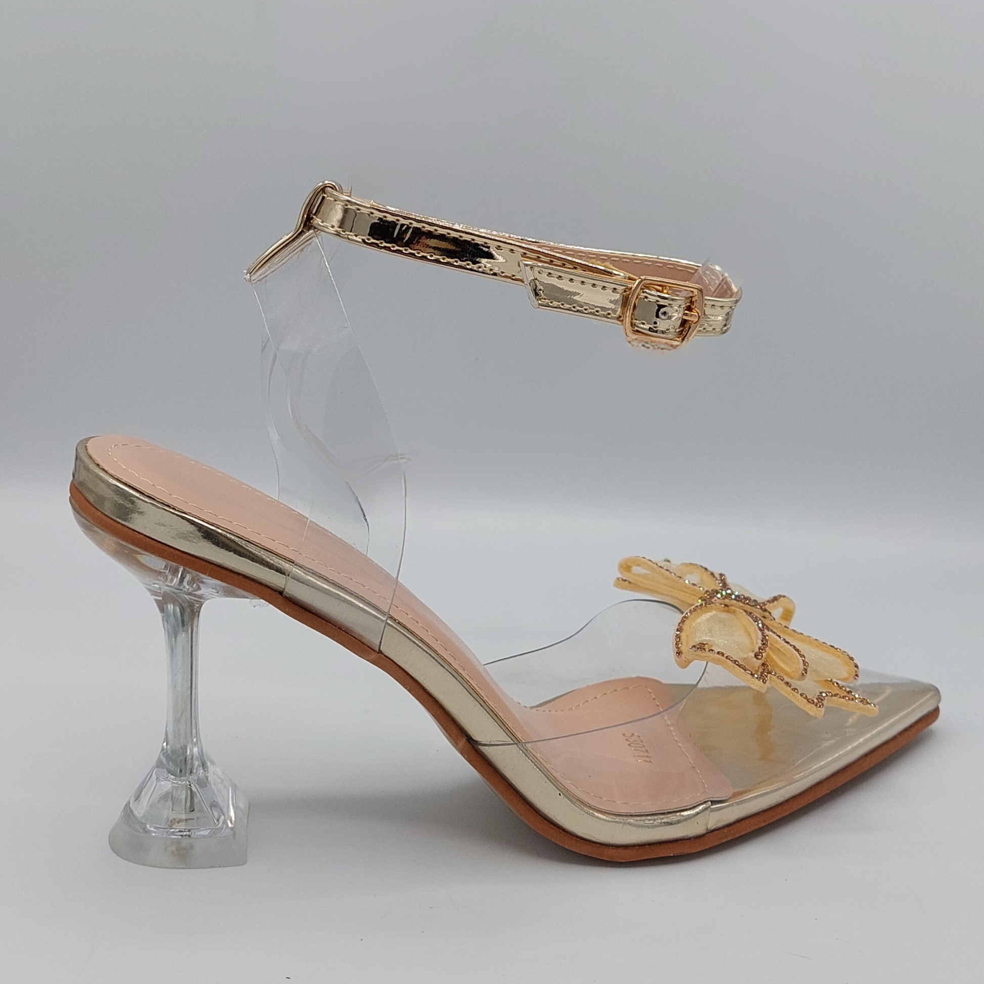 Front view of women's perspex court shoe with diamante brooch detail in gold, an elegant and stylish choice for London occasions.