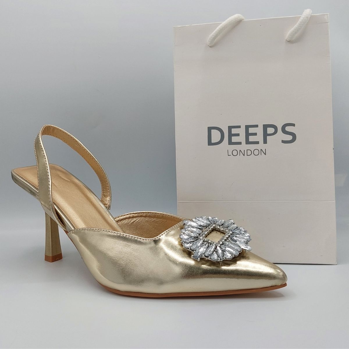 Front view of women's perspex court shoe with diamante brooch detail in Gold PU, an elegant and stylish choice for London occasions.