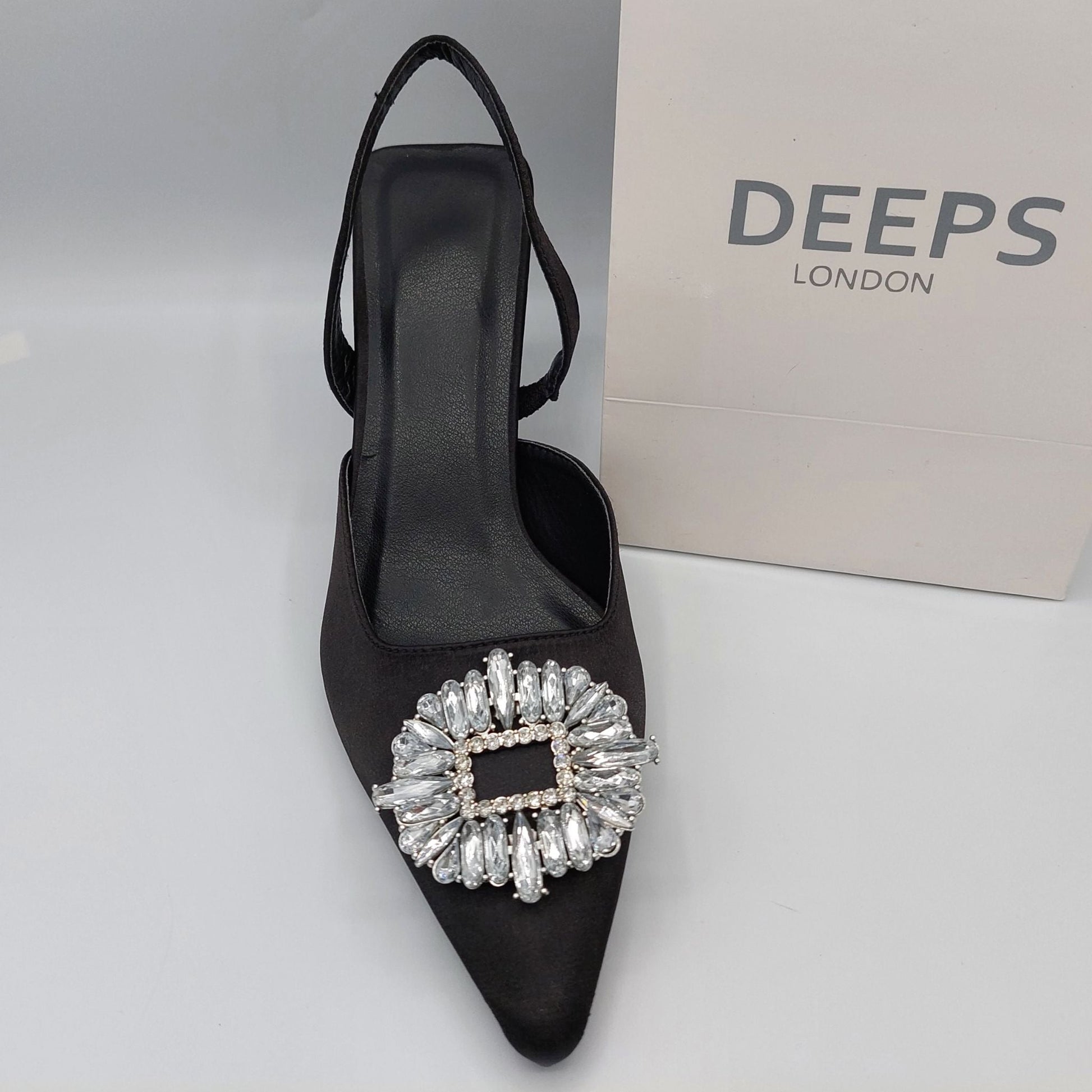 Woman's foot wearing stylish perspex court shoe with diamante brooch detail in Black Satin, a comfortable and fashionable choice for London events.
