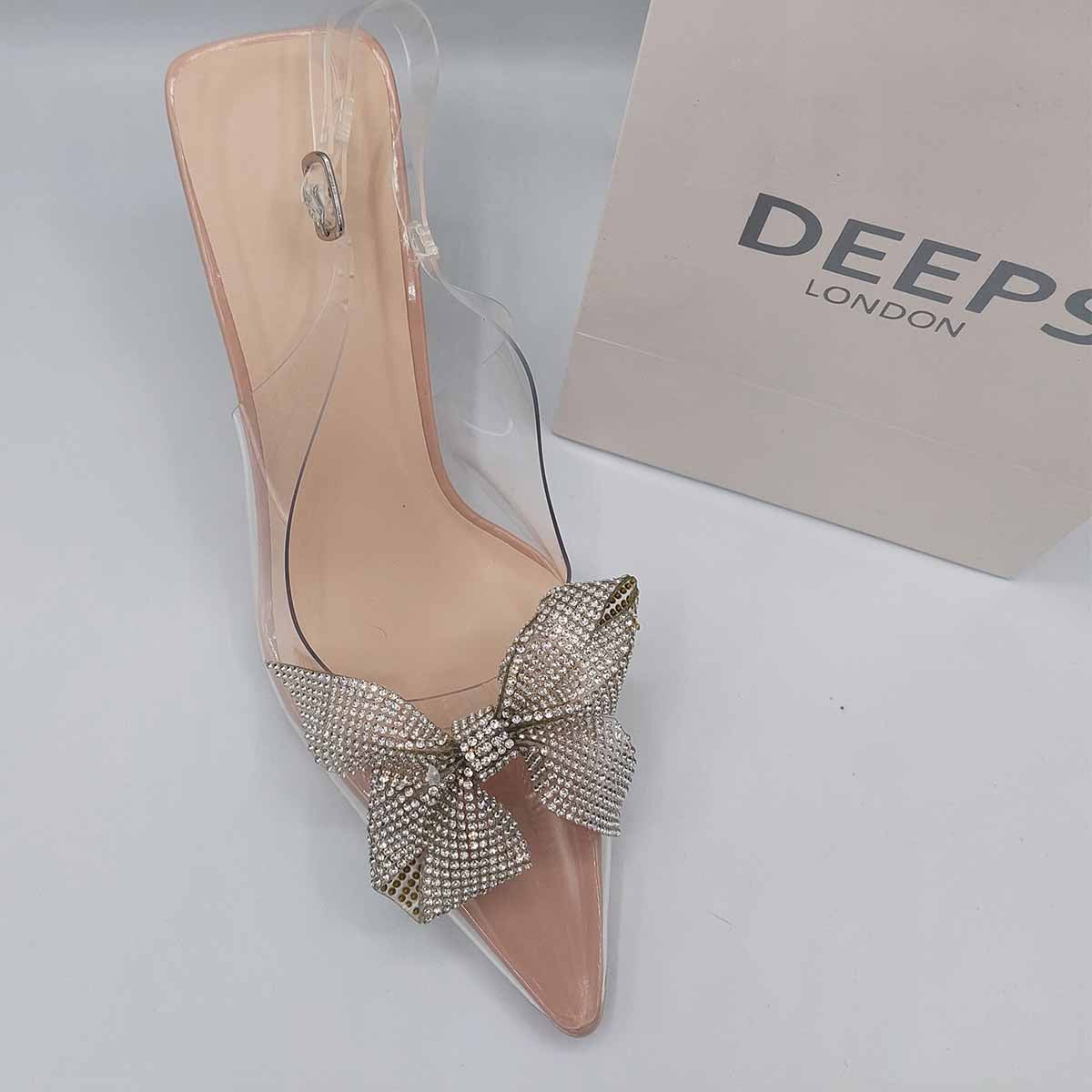 Woman's foot wearing stylish perspex court shoe with diamante brooch detail in silver, a comfortable and fashionable choice for London events.