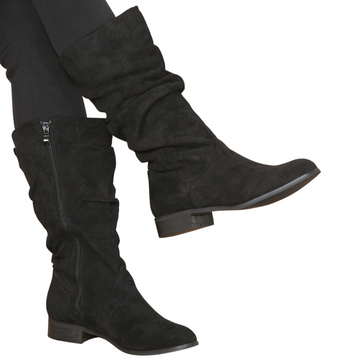 Woman's leg wearing stylish black suede ruched knee high boots with a side zip, a comfortable and fashionable choice for London life.