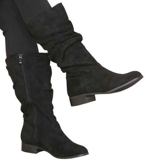 Woman's leg wearing stylish black suede ruched knee high boots with a side zip, a comfortable and fashionable choice for London life.