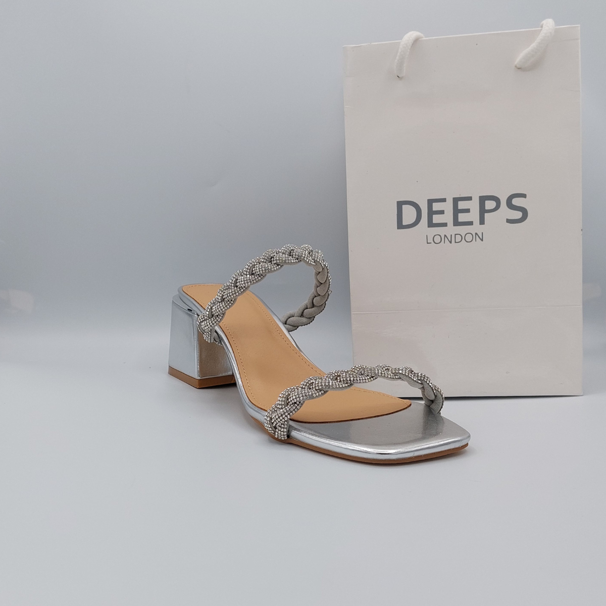 Woman's foot wearing stylish Deeps London silver plaited gemstone band block heel mule, a comfortable and fashionable choice for London events