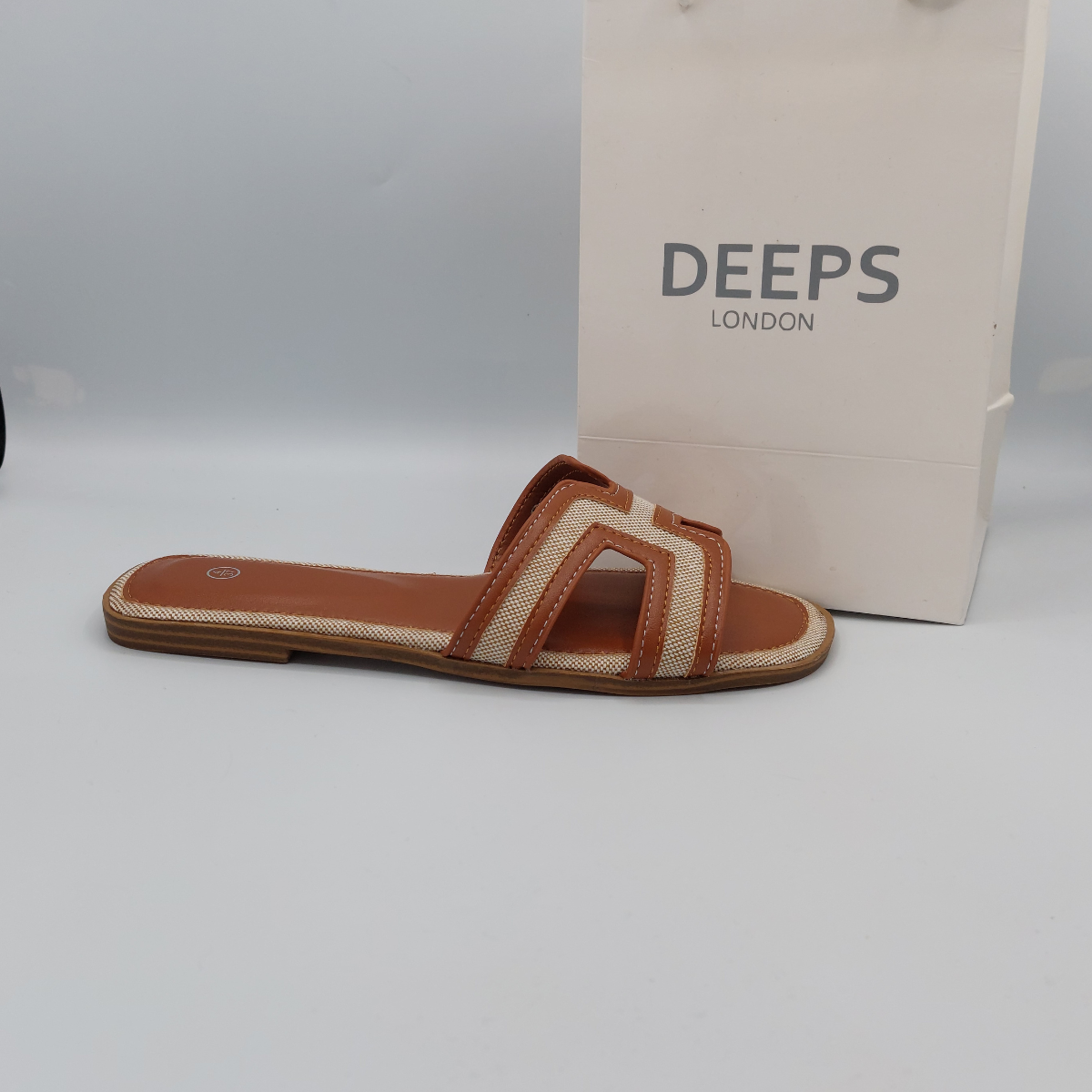 Side view of womens tan and beige flat sandals