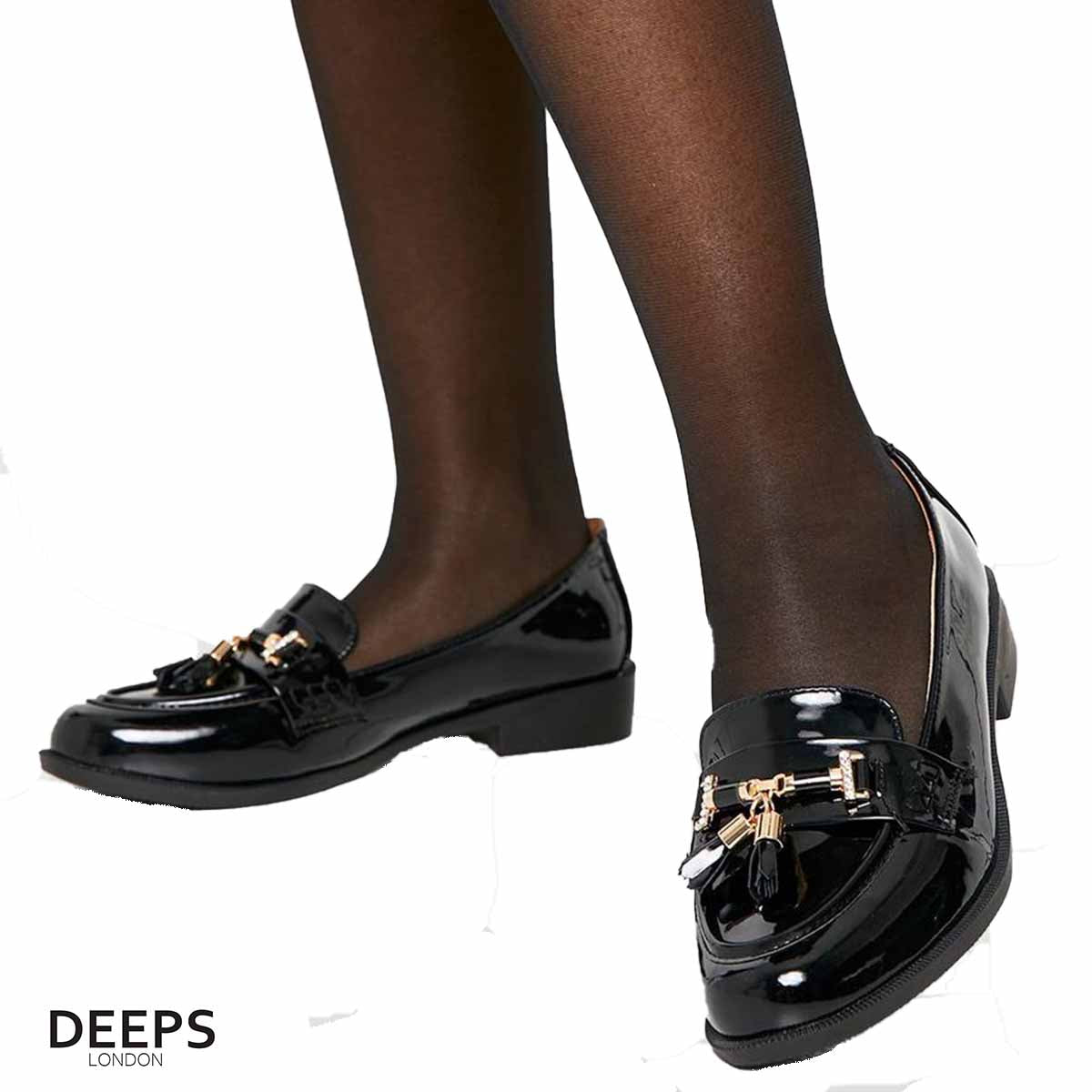 Woman's foot wearing stylish black classic slip-on loafers with a gold bar and tassels, a comfortable and fashionable choice for London life.