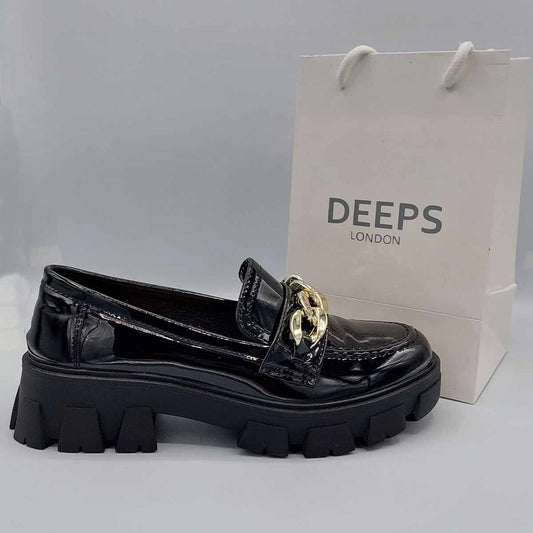 Front view of women's black patent flat loafer with a chunky platform and chain detail, a bold statement shoe in London.