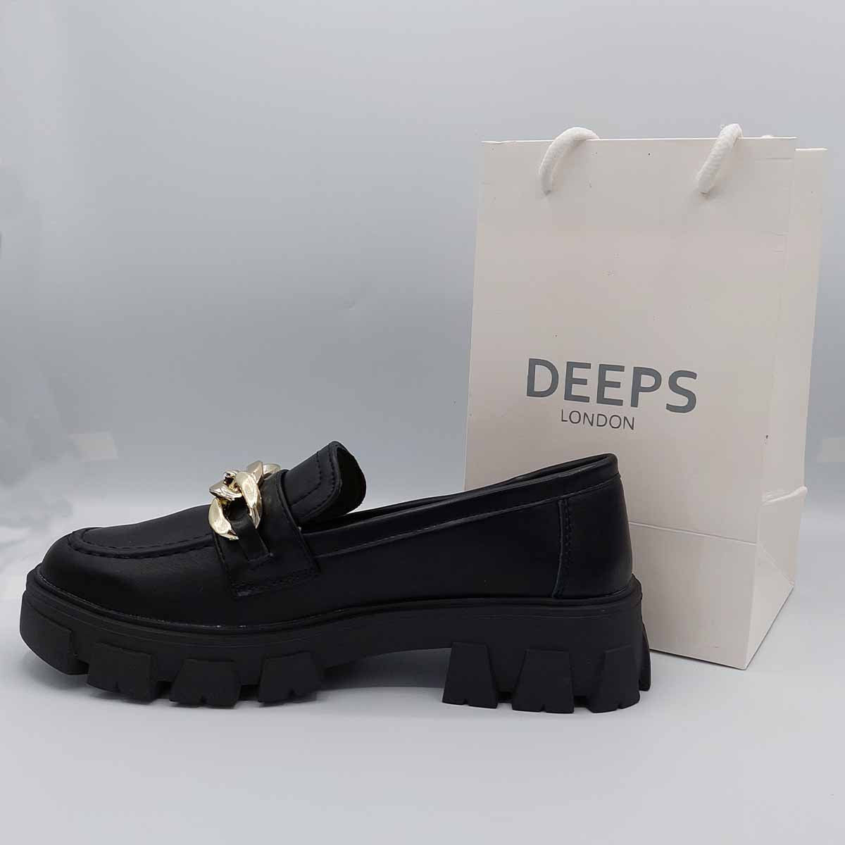 Woman's foot wearing stylish black PU flat loafers with a chunky platform and chain detail, a confident and comfortable footwear choice for London life.