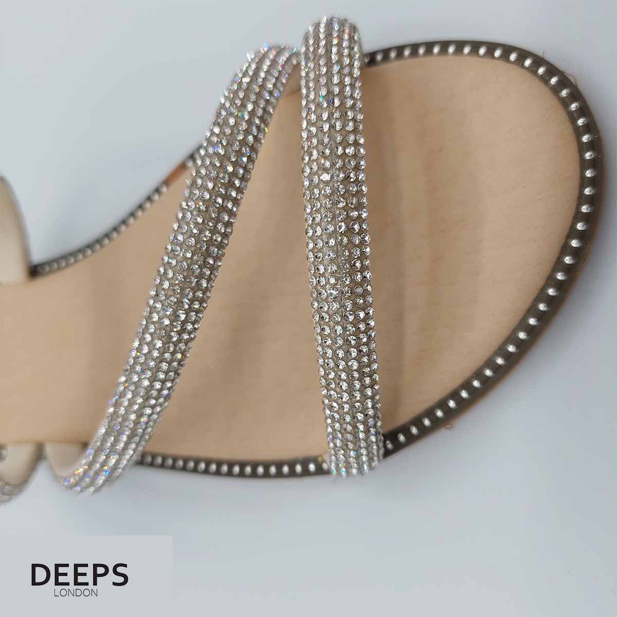 Close-up of the sparkly embellishments on the cross straps of women's flat slider sandals in beige, highlighting their glamorous features from DeepsLondon.