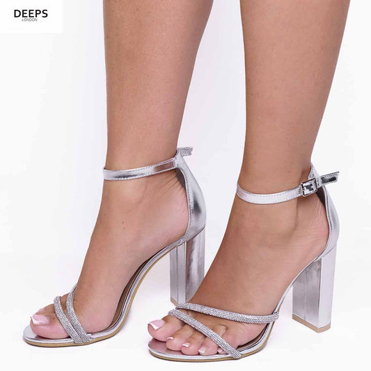 Woman's foot wearing stylish Imera double diamante strap block heel sandals in silver metallic, a fashionable and glamorous choice for London events from DeepsLondon.
