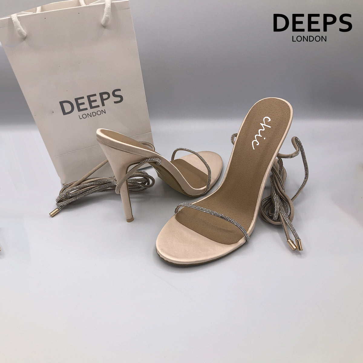 Side profile of women's Nomi satin rhinestone lace-up heels in champagne, showcasing the high heel and sparkling lace-up detailing for London fashion.