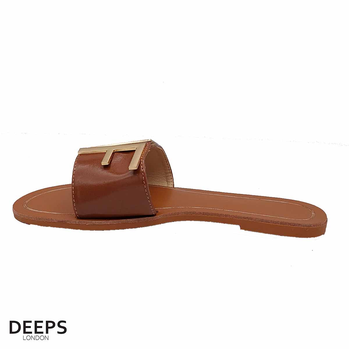 Woman's foot wearing stylish brown open toe flat slider sandals with a gold bar, a comfortable and fashionable choice for London life.
