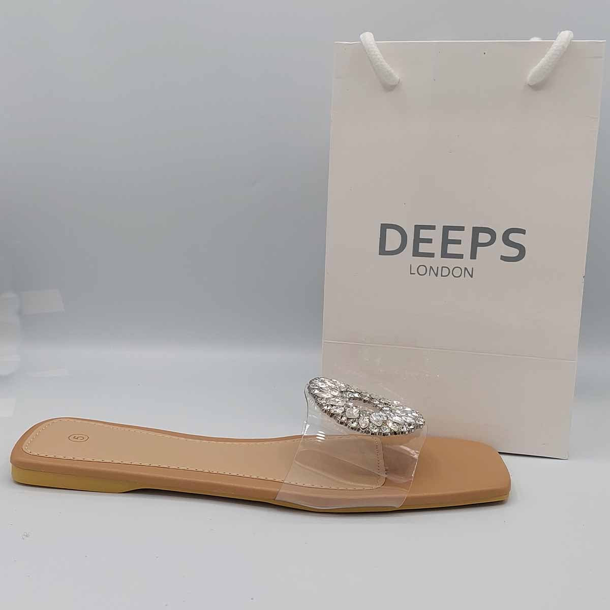 Close-up of the dazzling diamante embellishments on the beige perspex strap of these stylish flat slider sandals, adding a touch of London sparkle.