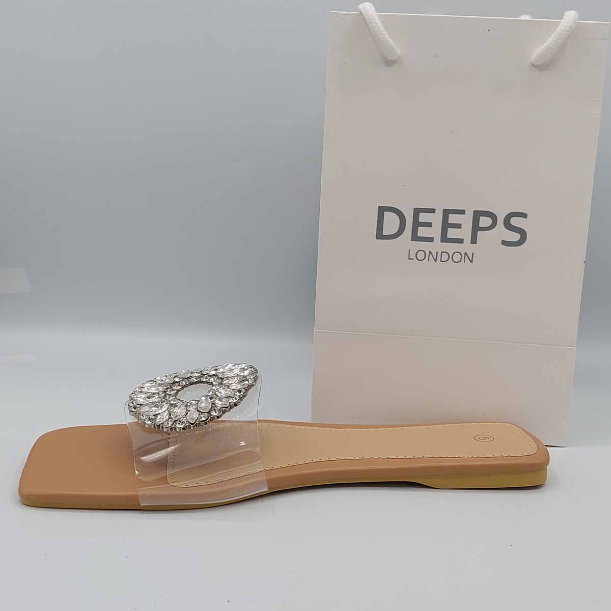 Woman's foot wearing chic beige perspex flat slider sandals with diamante detail, a fashionable and comfortable option for London life.