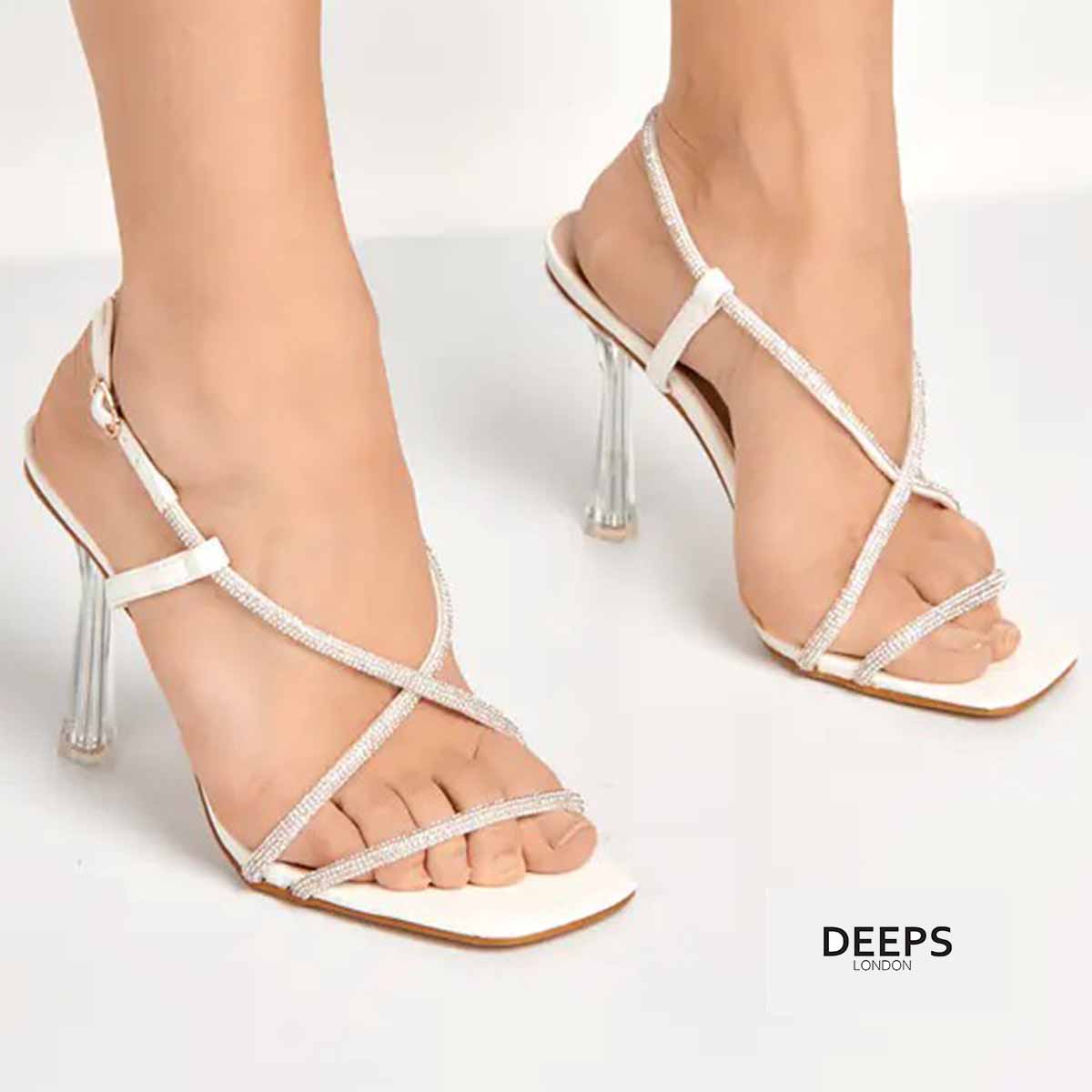 Woman's foot wearing stylish Wilde strappy diamante design stiletto heels with clear perspex heel in white, a fashionable and glamorous choice for London events from DeepsLondon.